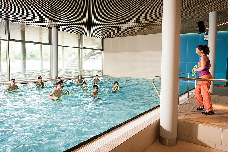 Frau gibt Übungen für Kinder im Schwimmbecken vor
