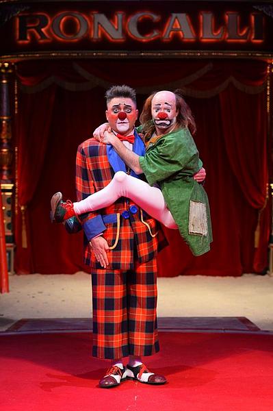 Ein wütend aussehender Clown trägt einen verängstigten Clown auf dem Arm