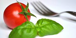 Tomate, Basilikumblätter und Gabel auf weißem Untergrund