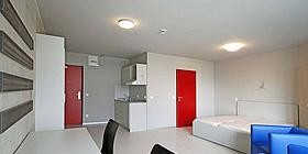 base 11 Pärchen Loft Pärchen-Appartment im Studentenwohnheim base 11, rote Einganstür und rote Türe zum Badezimmer, Raum ansonsten in hellem Weiß gehalten. weißes modernes Doppelbett, kornblaue Sitzmöbel. Doppelschreibtisch mit schwarzen Bürosesseln.