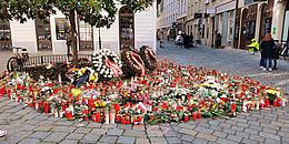 Ein Meer von Kerzen und Blumen ist herzförmig vor drei Kränzen, die neben einem Baum lehnen, aufgestellt worden.