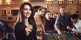 Junge Frau vor einem Roulette Tisch mit weiteren Menschen im Hintergrund