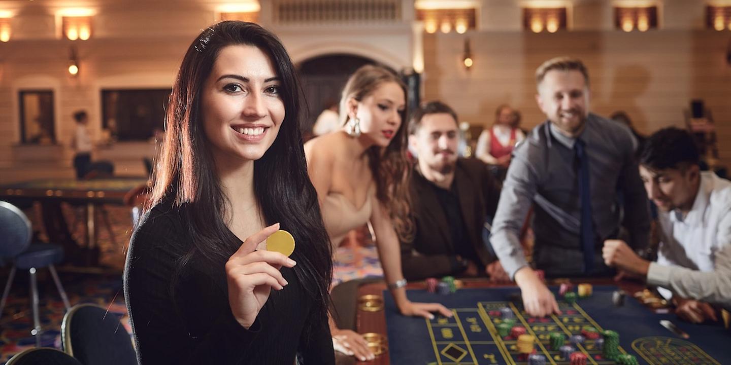 Junge Frau vor einem Roulette Tisch mit weiteren Menschen im Hintergrund