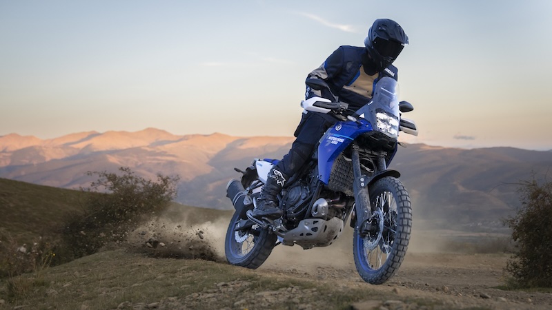 Yamaha Ténéré 700 2025 – Adventure-Bike mit Dakar-DNA, Offroad Biker im Hintergrund mit karger Bergkette