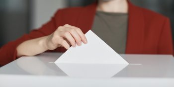 Frau wirft Wahlzettel in die Wahlurne.
