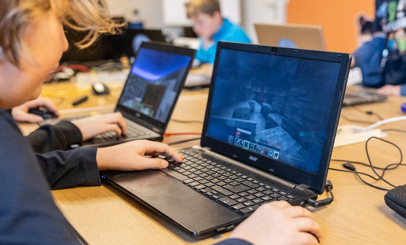 Kind sitzt an Tisch mit Laptop und spielt Minecraft