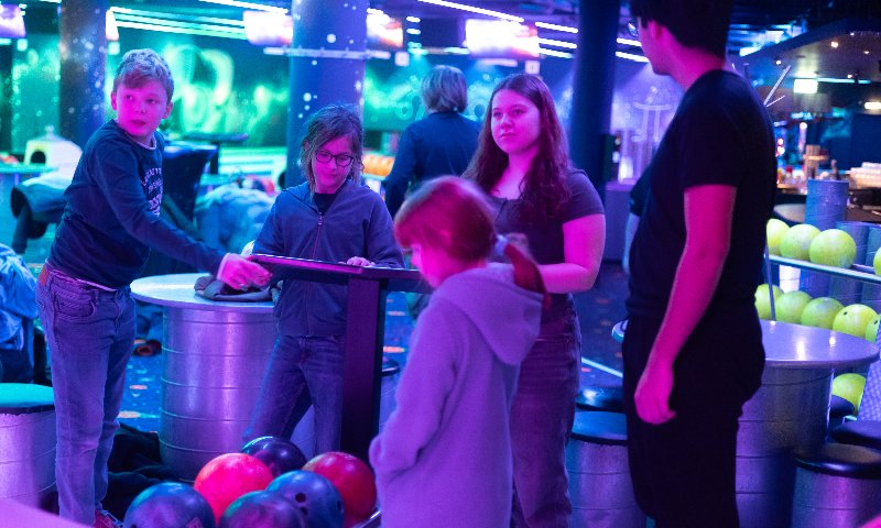 Kinder gehen mit ihrem Betreuer des Feriencamps eine Partie Bowlen