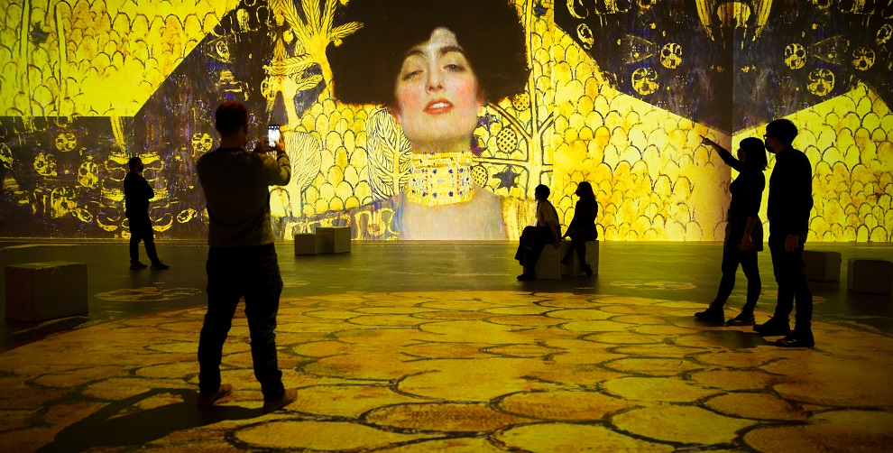Aufnahme der Ausstellung Klimt Experience, Menschen bewegen sich inmitten übergroßer Projektionen der Klimt-Werke
